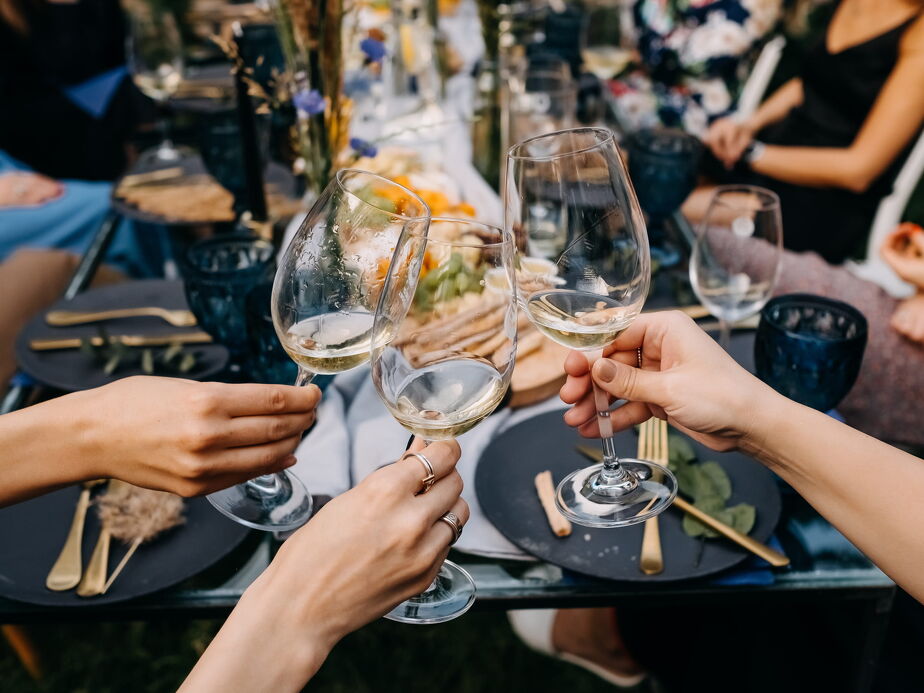 A close-up of hands clinking wine glasses in a toast at a stylish dinner table adorned with elegant plates, cutlery, and floral centrepieces.